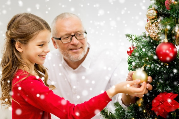 famiglia, vacanze, generazione e concetto di persone - ragazza sorridente con il nonno che decora l'albero di natale a casa