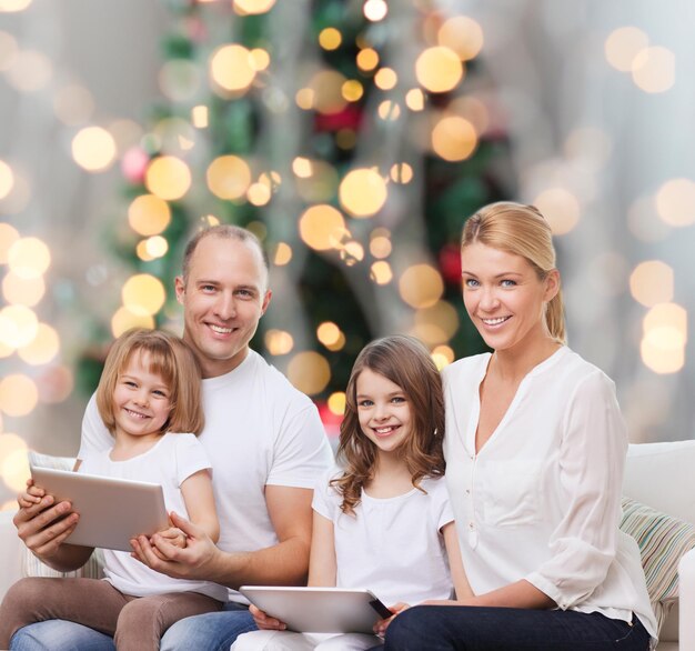 famiglia, vacanze, tecnologia e persone - madre, padre e bambine sorridenti con computer tablet pc su sfondo di luci albero di natale