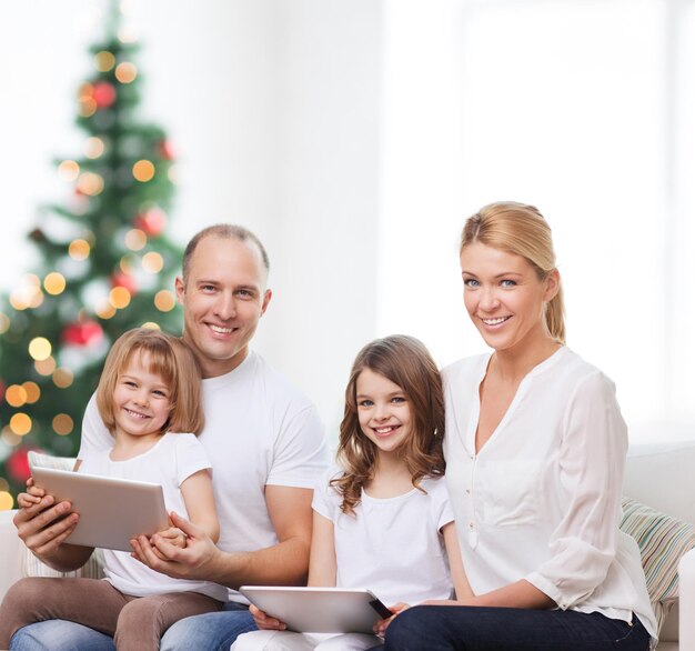 famiglia, vacanze, tecnologia e persone - madre, padre e bambine sorridenti con computer tablet pc su sfondo soggiorno e albero di natale