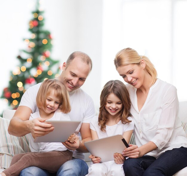 famiglia, vacanze, tecnologia e persone - madre, padre e bambine sorridenti con computer tablet pc su sfondo soggiorno e albero di natale