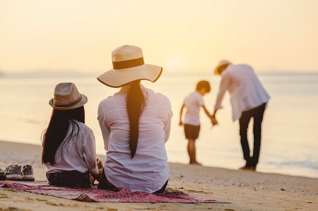 Famiglia, viaggi, spiaggia, relax, stile di vita, concetto di vacanza. Genitori e figli che in vacanza si godono un picnic in spiaggia al tramonto.