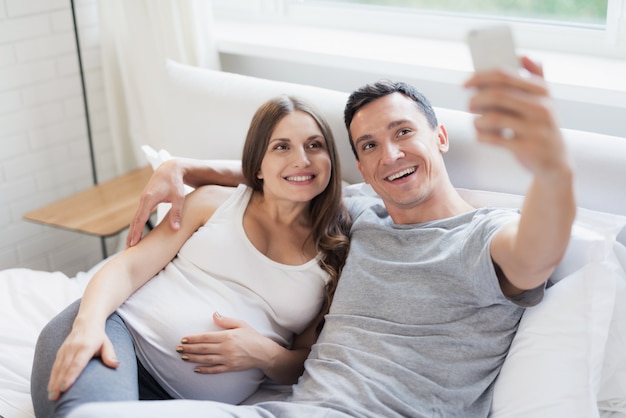 Family Selfie su Smartphone. Guy Hugs Pregnant.