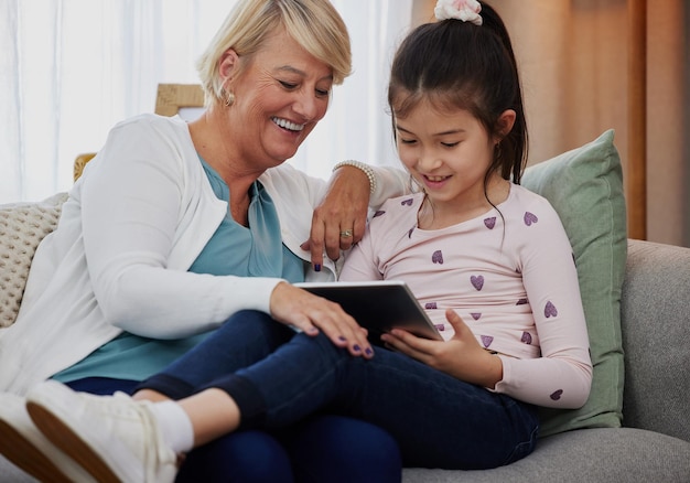 Fammi vedere il tuo punteggio Foto di un'adorabile bambina che usa una tavoletta digitale mentre è seduta a casa con sua nonna