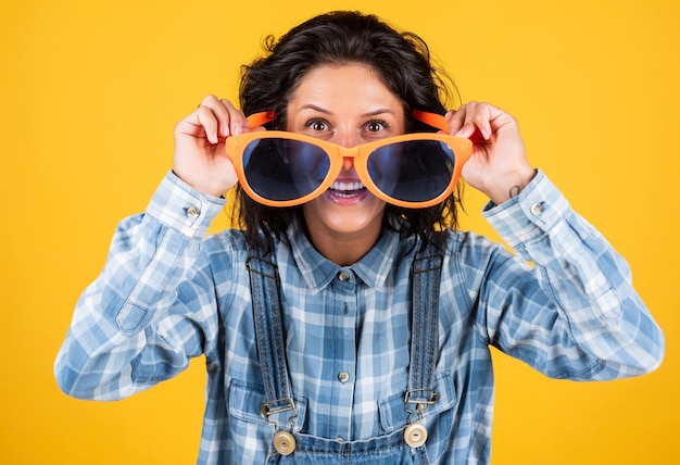 Fammi vedere la ragazza delle feste su sfondo giallo sorriso gioioso e affascinante studentessa che si diverte Moda ritratto bella giovane donna hipster donna in occhiali da festa divertenti tendenze casual e denim