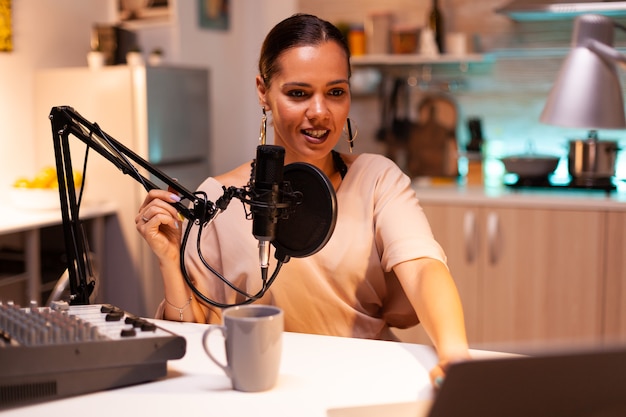 Famosa donna con microfono professionale durante la registrazione di podcast per i social media. La trasmissione online di produzione in onda mostra l'host in streaming di contenuti live, registrando social media digitali.