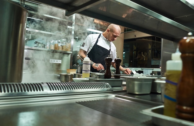 Famoso chef in grembiule nero che lavora nella cucina di un ristorante. Concetto di cibo