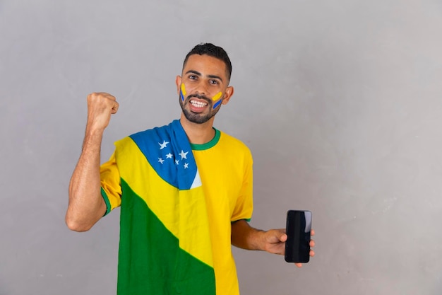 Fan afro-brasiliano che tiene uno smartphone con schermo vuoto con spazio libero per il testo che celebra la vittoria