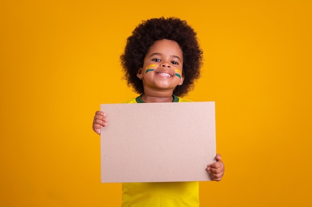Fan brasiliana adorabile della piccola ragazza afro che tiene carta in bianco con lo spazio della copia
