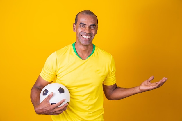 Fan brasiliano uomo che tiene pallone da calcio con copia spazio su sfondo giallo