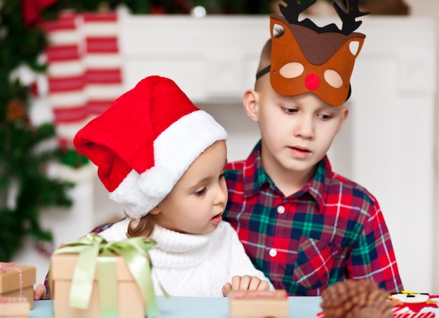 Fanny kids ragazza e ragazzo in berretto da Babbo Natale e maschera di cervo si congratulano a vicenda Buon Natale e Felice Anno Nuovo.