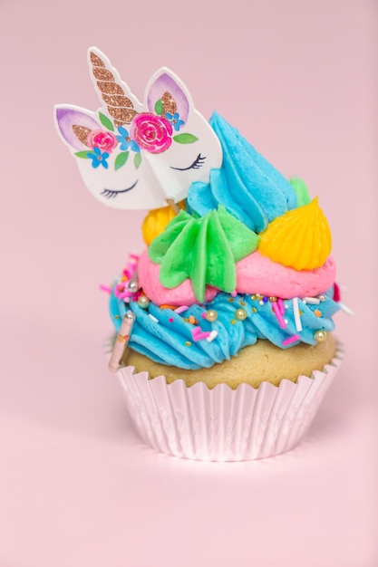 Fantasia di cupcakes con unicorno con glassa di crema di burro multicolore e topper per cupcake con unicorno su sfondo rosa.