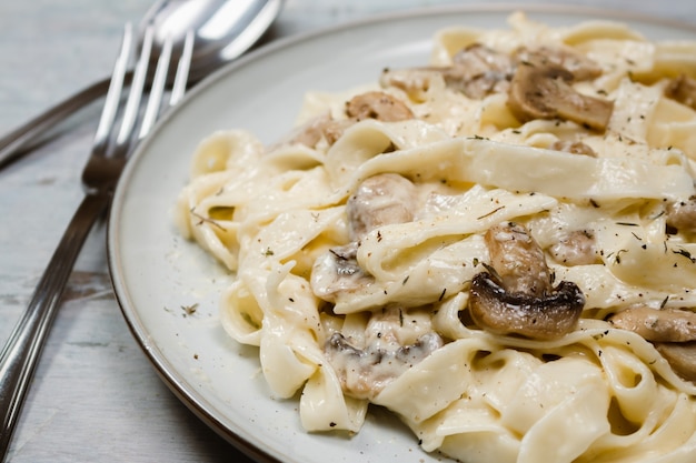 Fantasia di fettuccine biologiche con salsa cremosa ai funghi Alfredo. Superficie rustica.