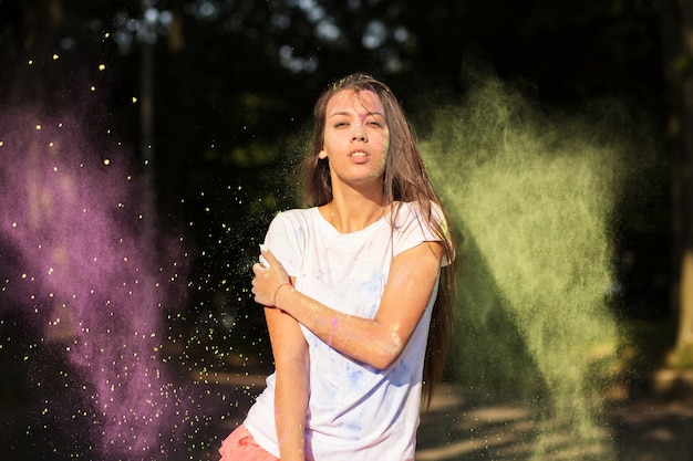 Fantastica modella asiatica abbronzata vestita con una camicia bianca, che gioca con la vernice Holi verde e viola