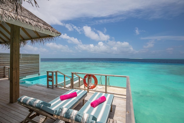 Fantastica villa sull'acqua, terrazza con vista mare e cielo, lettini prendisole, sedie sotto l'ombrellone, resort di lusso con piscina