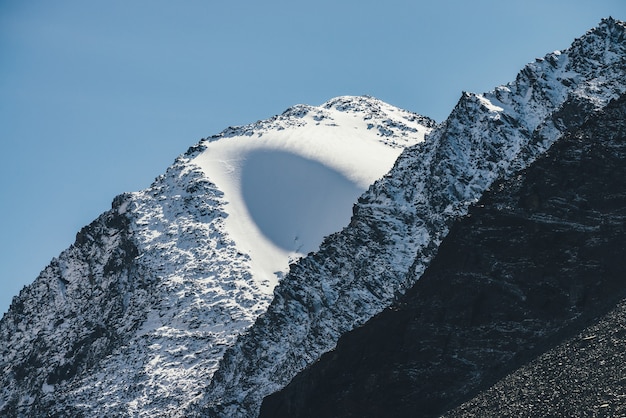 Fantastico paesaggio di montagna con neve bianca su rocce nere nel cielo blu. Atmosferico scenario alpino con sfera di neve sulla cima della montagna al sole. Bellissimo picco di neve a forma di sfera insolita alla luce del sole.