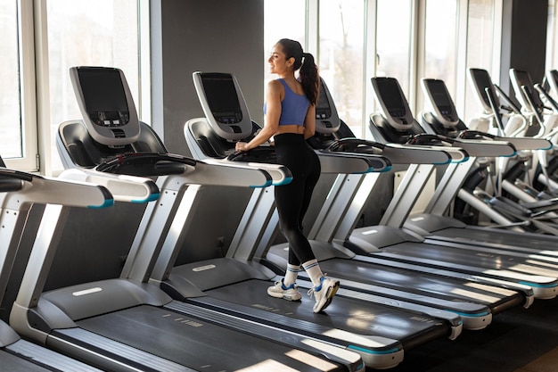 Fare cardio allenamento sport donna che lavora sul tapis roulant in palestra al mattino guardando alla finestra