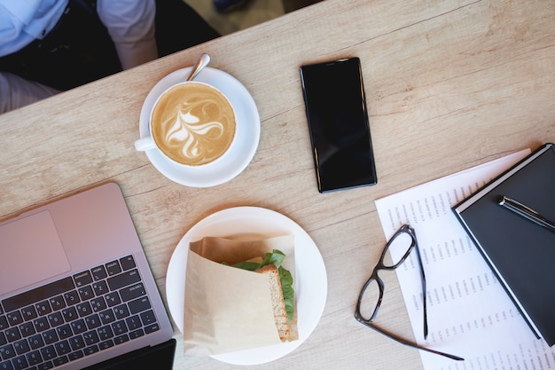 Fare colazione tazza di caffè cappuccino sandwich laptop e smartphone sul tavolo di legno in cafe