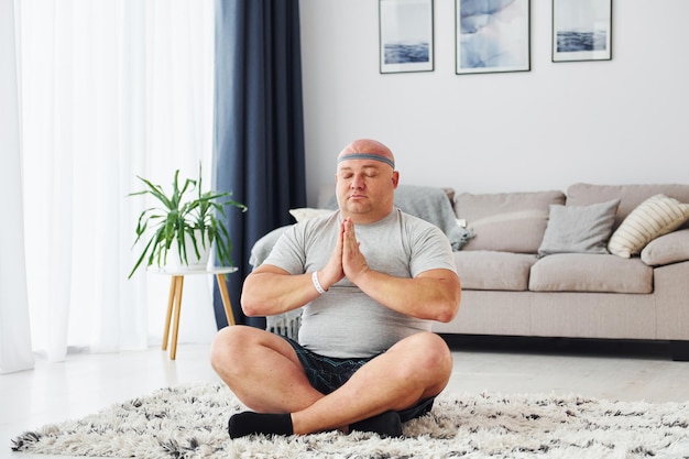 Fare esercizi di yoga Divertente uomo sovrappeso in abiti casual è in casa a casa