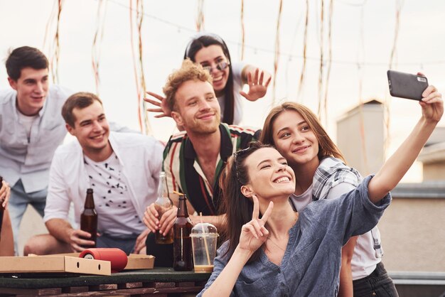 Fare foto Pizza deliziosa Un gruppo di giovani in abiti casual organizzano una festa sul tetto insieme durante il giorno