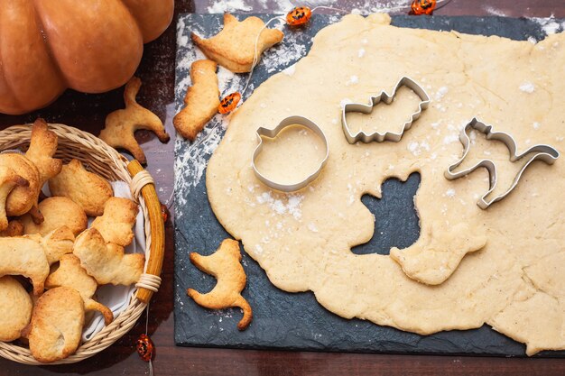 Fare i biscotti per Halloween. Ritaglia i biscotti dall'impasto a forma di zucca, gatto, fantasma e pipistrello.