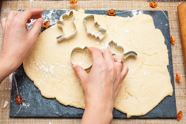 Fare i biscotti per Halloween. Una donna ritaglia dall'impasto dei biscotti a forma di zucca, gatto, fantasma e pipistrello.