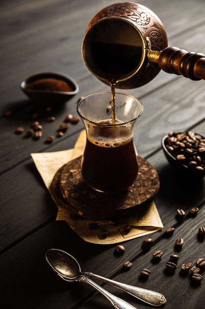 Fare il caffè a cezve. Fagioli, caffè macinato, versare il caffè dal cezve nel bicchiere. Fondale in legno.