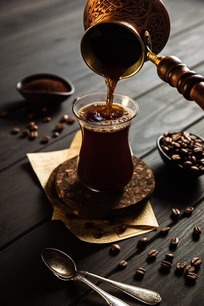 Fare il caffè a cezve. Fagioli, caffè macinato, versare il caffè dal cezve nel bicchiere. Fondale in legno.