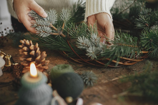 Fare la corona di Natale da vicino Mani che tengono il ramo di abete su sfondo rustico Workshop invernale