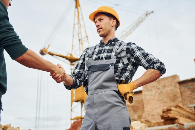 Fare la stretta di mano Due operai edili in uniforme e equipaggiamento di sicurezza hanno un lavoro per costruire insieme