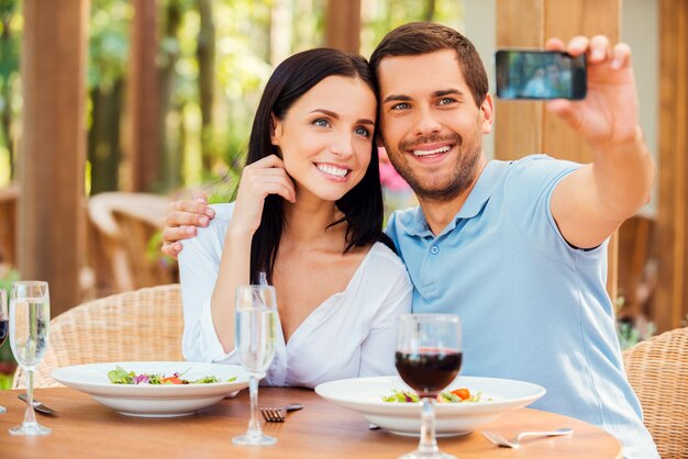 Fare selfie al ristorante. Bella giovane coppia di innamorati che fa selfie con il telefono cellulare e sorride mentre si rilassa insieme nel ristorante all'aperto