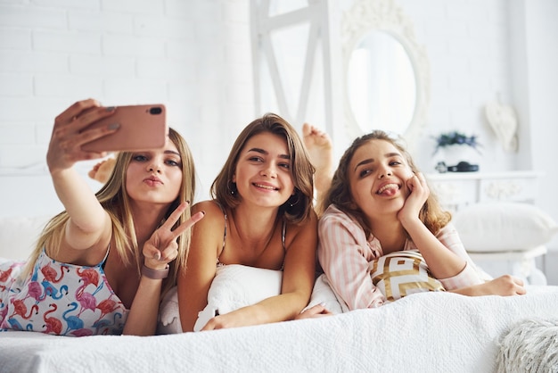 Fare selfie usando il telefono rosa. Felici amiche che si divertono al pigiama party in camera da letto.