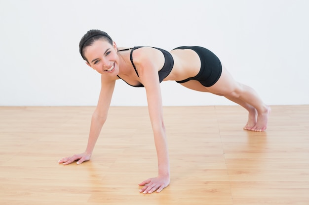 Fare sportivo sorridente della donna spinge aumenta nello studio di forma fisica