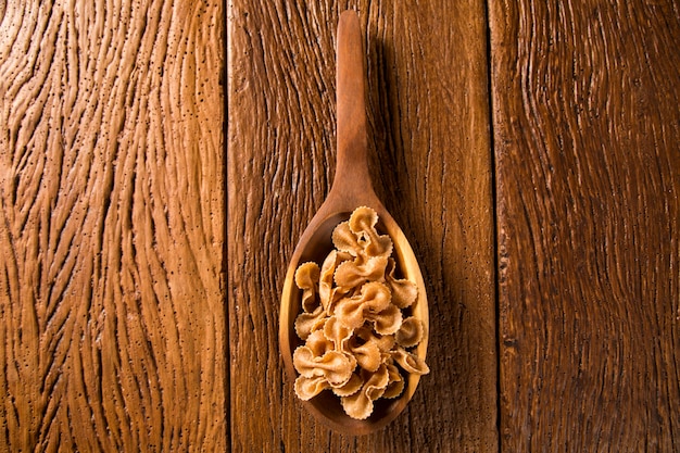 Farfalle crude o pasta farfallino sul cucchiaio di legno. Pasta integrale su un tavolo di legno