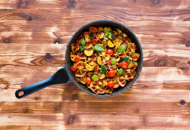 Farfalle di pasta italiana in salsa di pomodoro e vari tipi di verdure su un tavolo di legno