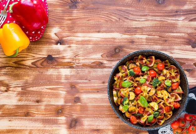 Farfalle di pasta italiana in salsa di pomodoro e vari tipi di verdure su un tavolo di legno