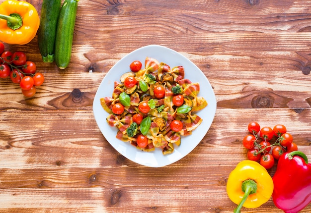 Farfalle di pasta italiana in salsa di pomodoro e vari tipi di verdure su un tavolo di legno