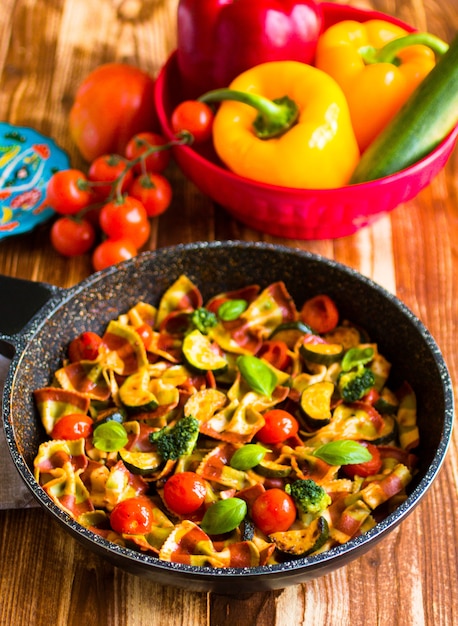 Farfalle di pasta italiana in salsa di pomodoro e vari tipi di verdure su un tavolo di legno