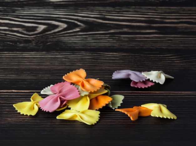 Farfalle o fiocchi di pasta italiana colorata secca su fondo di legno scuro. Con copia spazio