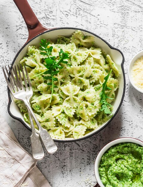 Farfalle vegetariane di pasta con pesto di broccoli in una padella di ghisa sul tavolo luminoso vista dall'alto