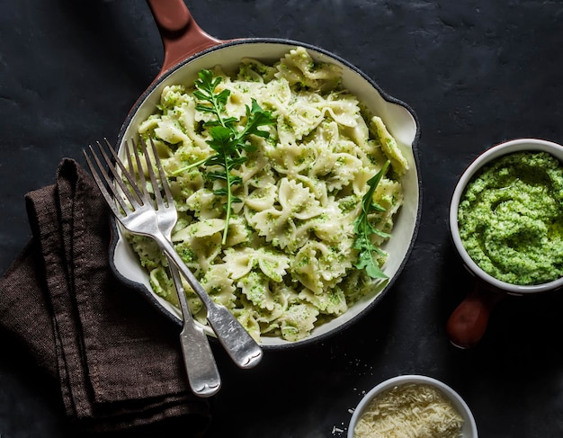 Farfalle vegetariane di pasta con pesto di broccoli in una padella di ghisa sul tavolo scuro vista dall'alto