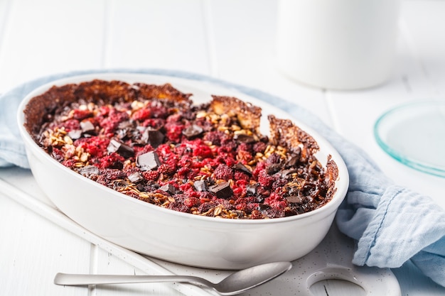 Farina d'avena al forno con frutti di bosco e cioccolato in un piatto bianco