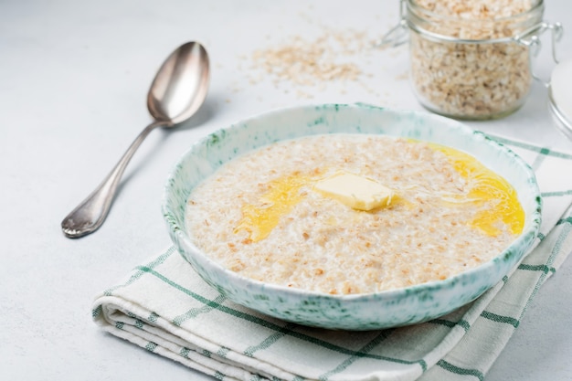 Farina d'avena con burro in un piatto di ceramica su una pietra chiara o cemento.