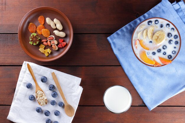 Farina d'avena con latte e frutta su fondo di legno Porridge di farina d'avena in una ciotola con frutta e mirtilli su tovagliolo di lino Vista dall'alto