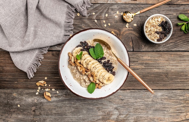 Farina d'avena con uvetta secca banana e noci decorate con menta Dieta sana colazione vegetariana o spuntino Mangiare pulito dieta vegan concetto di cibo vista dall'alto