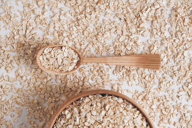 Farina d'avena in un piatto di legno e cucchiaio su sfondo bianco. Vista dall'alto. Copia, spazio vuoto per il testo