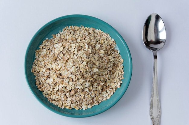 Farina d'avena in un piatto turchese mela verde e cucchiaio su sfondo bianco colazione sana hercules