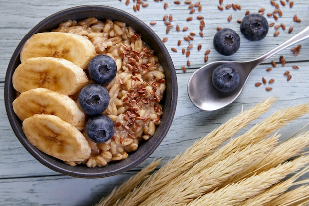 Farina d'avena integrale con mirtilli e fette di banana su un tavolo blu con un mazzo di farina d'avena e un asciugamano da cucina. Farinata di cereali per una dieta sana. Vista dall'alto. Disposizione piatta