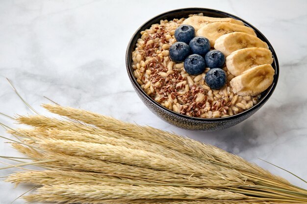 Farina d'avena integrale con semi di lino con mirtilli e fette di banana su un tavolo di marmo bianco. Energia e salute alimentare