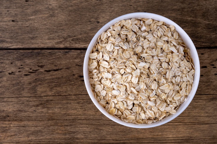 Foto farina d'avena laminata a secco in una ciotola su fondo di legno vista dall'alto