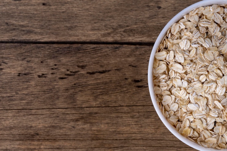 Foto farina d'avena laminata a secco in una ciotola su fondo di legno vista dall'alto